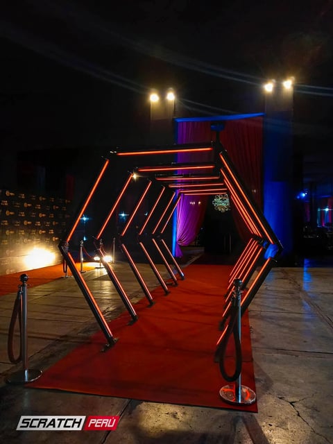 Túnel LED hexagonal rojo: Entrada impactante sobre alfombra roja, perfecta para eventos de gala y celebraciones.
