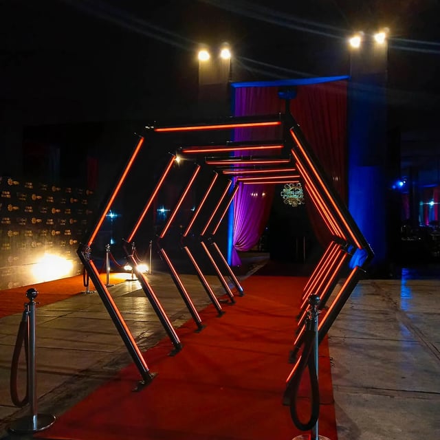 Túnel LED hexagonal rojo: Entrada impactante sobre alfombra roja, perfecta para eventos de gala y celebraciones.