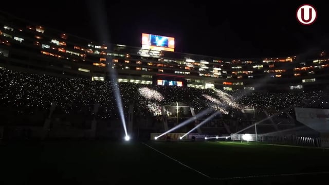 Vista nocturna del Estadio Monumental de Lima durante un partido de fútbol, con el campo iluminado por luces de cabezales móviles y las gradas llenas de aficionados que usan pulseras LED DMX inalámbricas sincronizadas con el juego