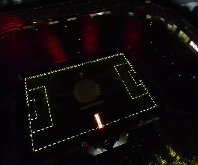 Vista general de un estadio de fútbol con el contorno de la estructura iluminado por píxeles LED y los espectadores usando brazaletes LED que se encienden y apagan según el desarrollo del partido, creando una atmósfera única y emocionante
