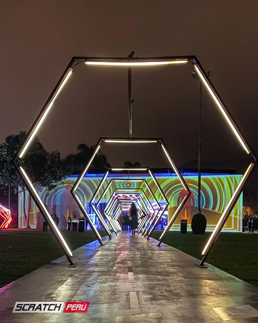 Túnel LED hexagonal blanco: Ambiente luminoso con personas ingresando al evento, creando una atmósfera festiva.