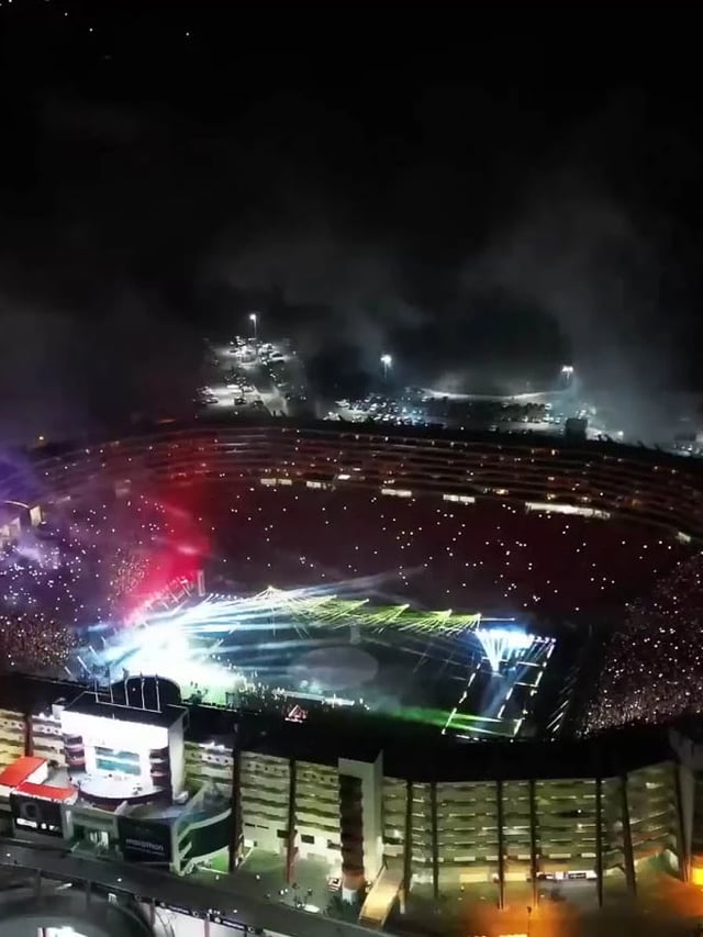 Vista desde el campo de fútbol de usuarios usando brazaletes inalámbricos luminosos en un evento deportivo, con los brazaletes creando un efecto de ola de luz y color en las gradas