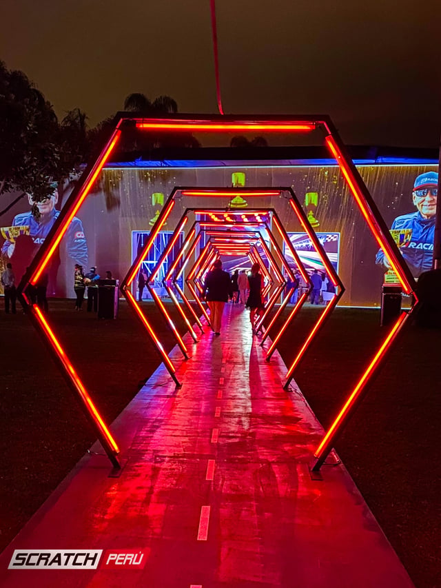 Túnel LED hexagonal rojo: Entrada dramática con personas ingresando al evento, capturando momentos memorables.
