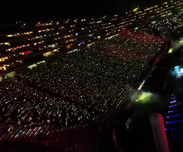 Vista panorámica de un estadio de fútbol lleno de espectadores que llevan pulseras LED DMX inalámbricas de diferentes colores, controladas en tiempo real para crear efectos visuales impresionantes