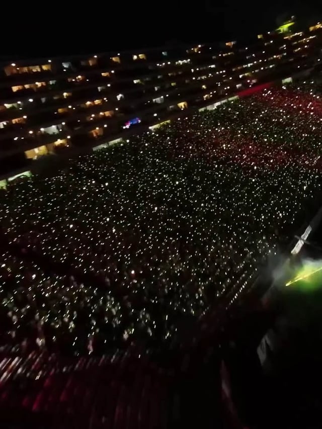 Vista panorámica de un estadio de fútbol lleno de espectadores que llevan pulseras LED DMX inalámbricas de diferentes colores, controladas en tiempo real para crear efectos visuales impresionantes